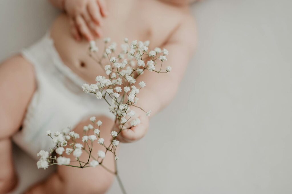 Portrait of a baby in a diaper delicately holding white flowers, emphasizing innocence.