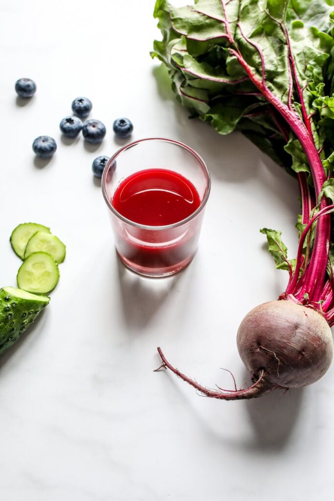 Overhead view of fresh beetroot juice with cucumber, blueberries, and beet on a white background.