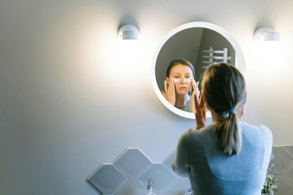 A woman applies under eye patches in a modern bathroom, emphasizing self-care.