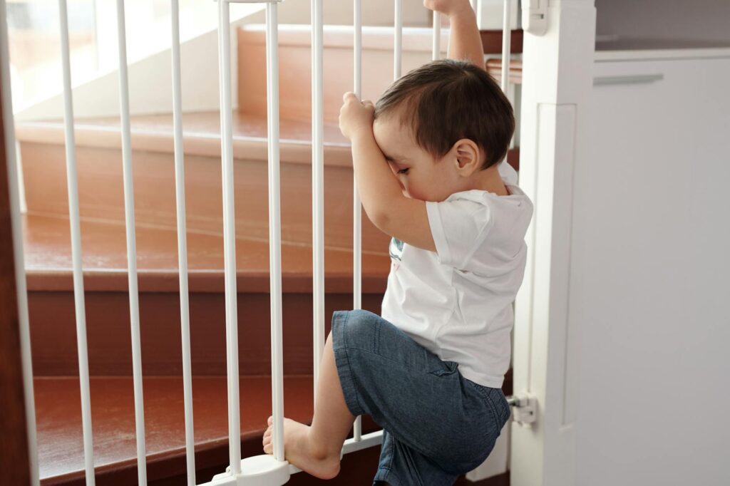 A curious toddler climbing a safety gate near stairs inside a home.