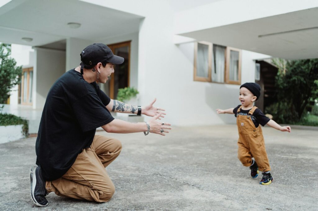 A father extends his arms as his joyful son runs towards him in an outdoor setting.