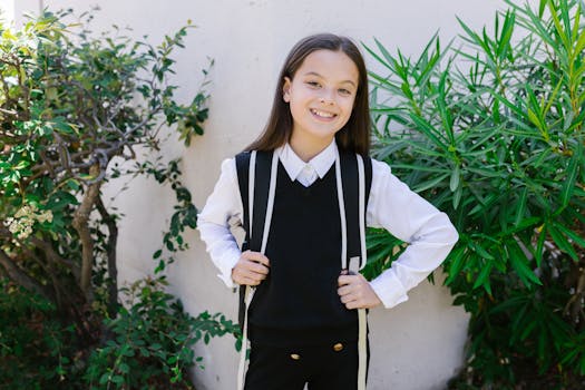 Young girl in school uniform smiling confidently outdoors with backpack.